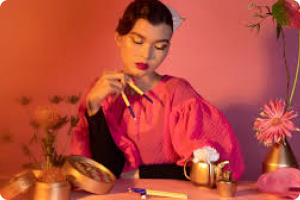 Woman wearing pink and styled hair holds two brushes in her hand and gazes down showing her eye make up